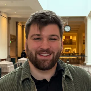 Portrait of Charlie Lindberg, smiling, wearing a dark shirt and olive jacket.