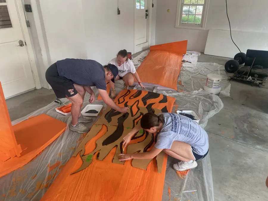 Painters using a cardboard stencil to add black tiger stripes to the orange wing.
